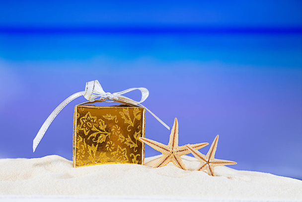 Zlatá krabička se žlutými hvězdami na tropické pláži oceánu. Vánoce, Nový rok, narozeninová dovolená v horkých zemích koncept pozadí. Kopírovat prostor - Fotografie, Obrázek