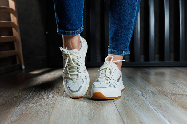 スレンダーな女性の足のクローズアップでジーンズと本革で作られた白いスニーカー. - 写真・画像