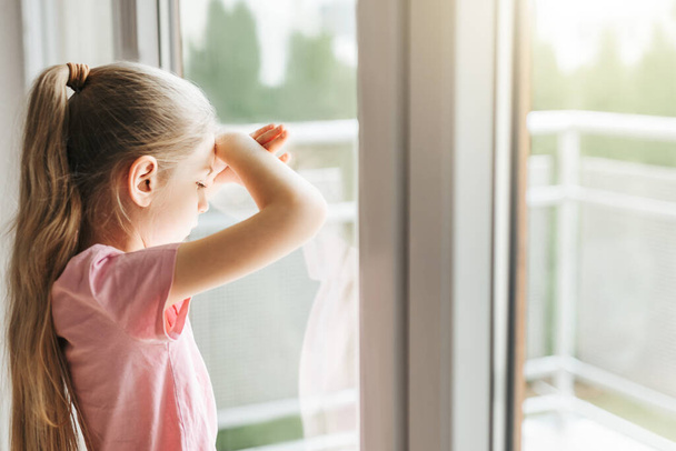 Lonely little girl  looking out window, standing at home alone.  - Photo, Image