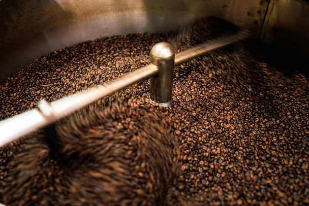 fresh coffee beans roasted spinning cover professional machine close up to soft focus  slow shutter speed because want to make motion blur of coffee beans detail concept, at factory chiang rai Thailand, angle view shot. - Фото, зображення