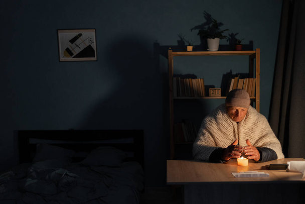 Älterer Mann ohne Strom zu Hause mit Kerze. Abschaltung von Heizung und Strom, Stromausfall, Stromausfall, Lastverlust oder Energiekrise. Kopierraum. - Foto, Bild