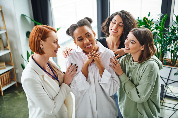 positieve psycholoog en multiraciale vrouwelijke vrienden knuffelen blij Afrikaans-Amerikaanse vrouw tijdens psychologische coaching, morele ondersteuning en geestelijke welzijn concept - Foto, afbeelding