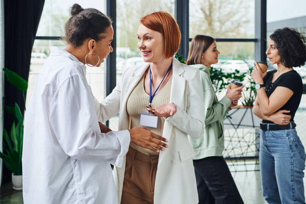 smiling redhead psychologist talking to young african american woman near multiethnic girlfriends drinking coffee to go on blurred background, motivation and supportive therapy concept - Photo, Image