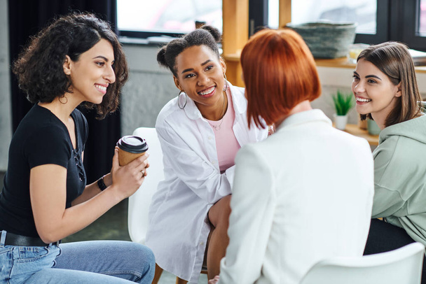 Kahve içen çok ırklı bir kadın terapi, anlayış, destek ve akıl sağlığı konsepti sırasında iyimser çoklu etnik kız arkadaşlarla birlikte oturup kızıl saçlı psikologları dinliyor. - Fotoğraf, Görsel