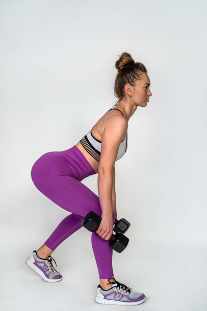 Beautiful young woman squats with dumbbells to pump the muscles of the buttocks isolated on a white background. beautiful figure healthy way to gain weight - Fotó, kép