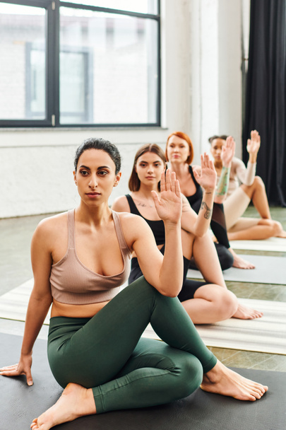 diverse group of multiethnic female friends in sportswear meditating while sitting in lord of fishes pose and looking away during yoga class in gym, wellness and mental health concept - Фото, зображення
