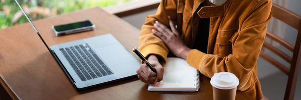Empresaria afroamericana leyendo datos de negocios en laptop y escribiendo notas en notebook. - Foto, imagen