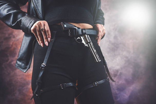dangerous slim woman in black outfit holding handgun pistol isolated on dark, crime concept - Foto, imagen