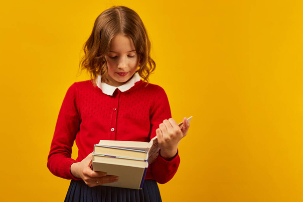 Portret van een gelukkig schoolmeisje dat een boek leest over gele studioachtergrond, onderwijsconcept, Terug naar School, kopieerruimte, Tiener meisje in schooluniform. - Foto, afbeelding