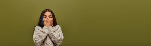 Módní předpuberťačka s obarvenými vlasy na sobě moderní útulný pletený svetr při zakrytí obličeje, baví a stojí izolovaně na zelené, banner, módní preteen se smyslem pro styl - Fotografie, Obrázek
