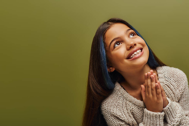 Portret uśmiechniętej nastolatki brunetki z farbowanymi włosami noszącej sweter z dzianiny podczas modlitewnego gestu dłoni i stojącej odizolowanej na zielonej, modnej nastolatce z poczuciem stylu - Zdjęcie, obraz