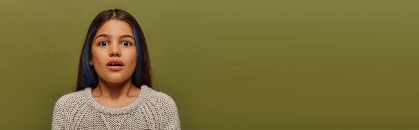 Retrato de niño preadolescente sorprendido con el pelo teñido con suéter de punto moderno y mirando a la cámara mientras está de pie aislado en verde, pancarta con espacio de copia, moda preadolescente moderna - Foto, imagen