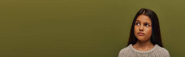 Retrato de chica morena preadolescente pensativa en suéter de punto de moda mirando hacia otro lado mientras está de pie aislado en verde con espacio para copiar, chica elegante en concepto de traje de otoño acogedor, pancarta  - Foto, imagen