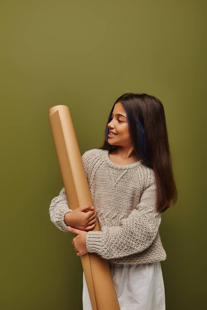 Радостный подросток с крашеными волосами в стильном и уютном осеннем трикотажном свитере, смотрящий на бумагу и стоящий изолированный на зеленом, девушка излучает осенние вибрации концепции - Фото, изображение