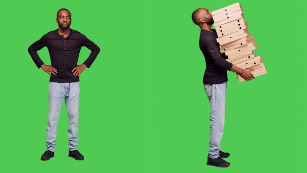 Modello maschio consegna grande mucchio di scatole di pizza in studio, portando un sacco di confezioni di cartone con ordine pasto da asporto. Uomo casual con fiducia in posa su sfondo schermo verde corpo pieno. - Foto, immagini