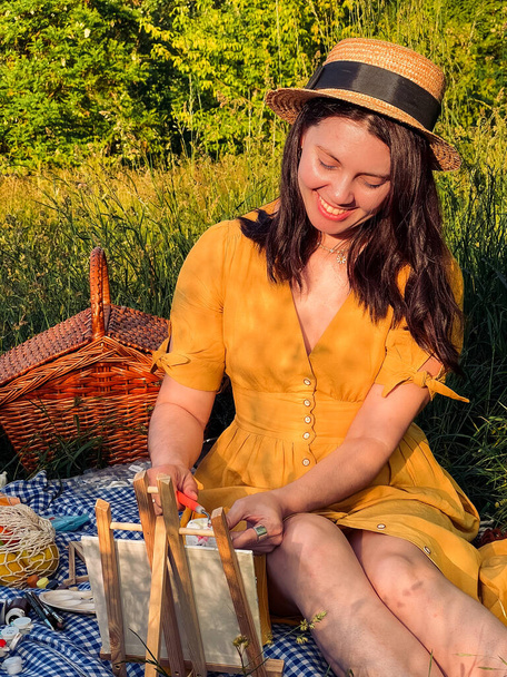 Piknik művészet: nő sárga ruhában és kalapban megengedi magának a szabadtéri festészet. - Fotó, kép