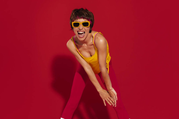 Excited young woman in retro styled sportswear having fun against red background - Φωτογραφία, εικόνα