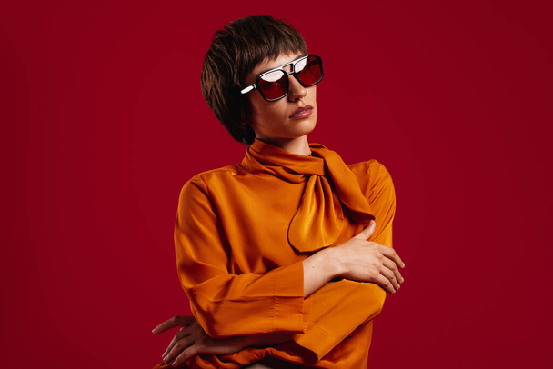 Portrait of beautiful young short hair woman in trendy glasses standing against red background - Foto, Imagem