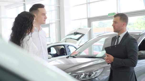 A car sales manager shows a new electric car in a car showroom. Car sales concept. - Metraje, vídeo