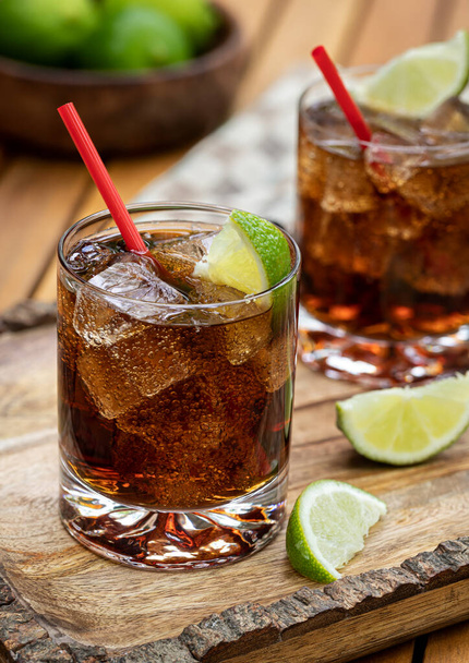 Rum and cola cocktail with ice and lime slices on rustic wooden tray - Foto, immagini