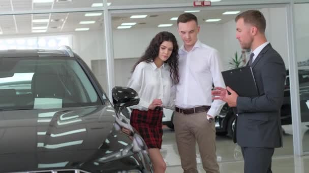 A happy young family buys a luxury car. Car sales manager showing a new car. Car sales concept. - Video