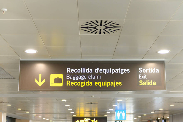 Багаж претензии и выход знак в аэропорту на Ибице, Испания. На вывеске написано "Багаж претендует и выезжает" на каталонском, английском и испанском языках.. - Фото, изображение