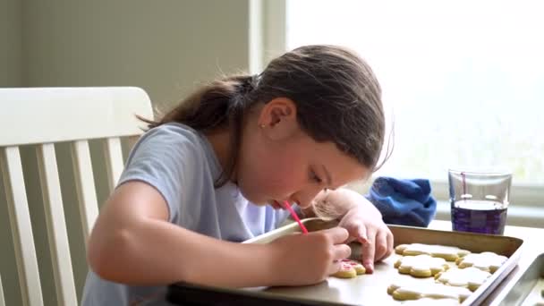 Une scène chaleureuse d'une petite fille écrivant avec soin Désolé sur les biscuits au sucre avec colorant alimentaire, les biscuits magnifiquement inondés de glaçage royal blanc. - Séquence, vidéo