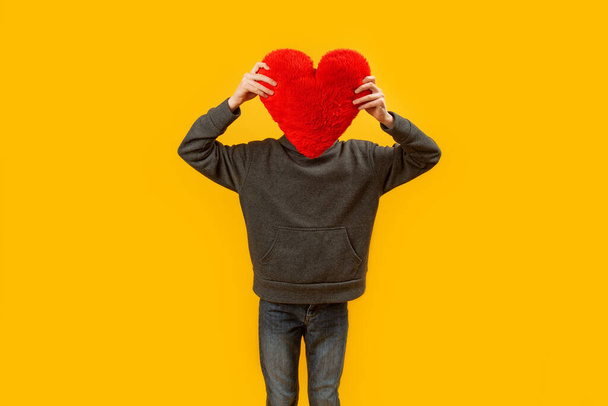Child holds red pillow in shape of heart. Man with plush heart instead of head. Copy space. Yellow background - Fotoğraf, Görsel
