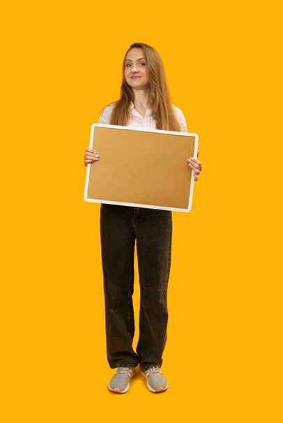 Young woman holds cork board on yellow background. Full-length portrait of woman with note board. Copy space - Fotoğraf, Görsel