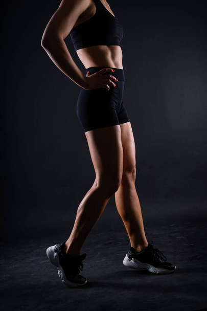 Cropped legs of a fit young woman with strong muscles over dark background - Valokuva, kuva