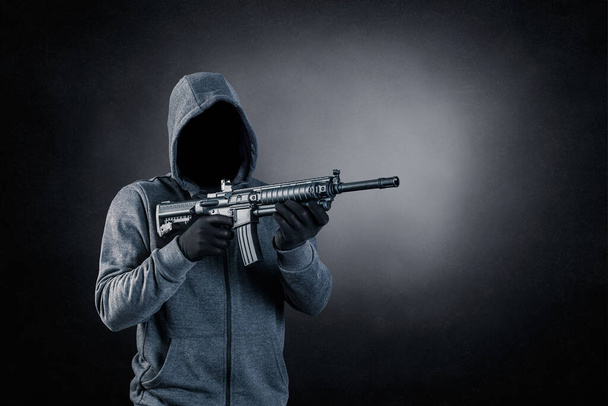 Hooded man with assault rifle over dark misty background - Фото, изображение