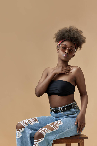 Portrait of young, beautiful, african woman with smooth, glowing skin, posing in top and sunglasses against studio background. Concept of natural beauty, skin care, health, fashion, wellness, ad - Foto, afbeelding