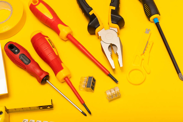Electrician equipment on yellow background with copy space.Top view.Electrician tool set.Multimeter, tester,screwdrivers,cutters,duct tape,lamps,tape measure and wires.Flet lay. - Zdjęcie, obraz