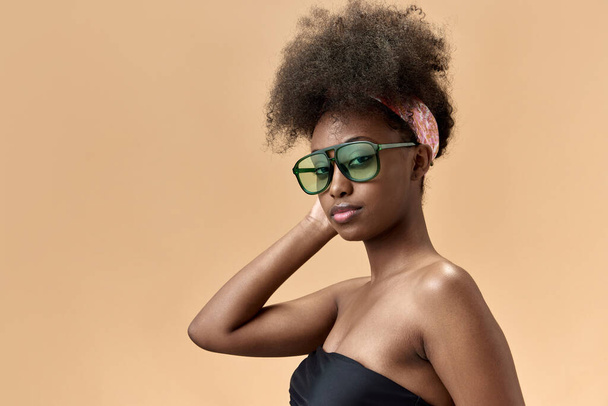 Portrait of young, stylish, beautiful, african woman in tredy sunglasses, top posing against studio background. Concept of natural beauty, skin care, health, fashion, wellness, ad - Photo, Image