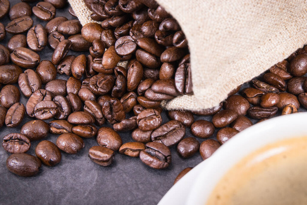 White glass cup of coffee and roasted dark fragrant coffee grains in jute bag - Фото, зображення