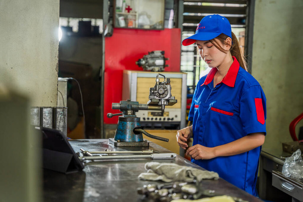 A female diesel engine mechanic in a blue uniform is working at the garage. Inspect and maintain the fuel pressure booster pump system and common rail injectors. - Фото, изображение