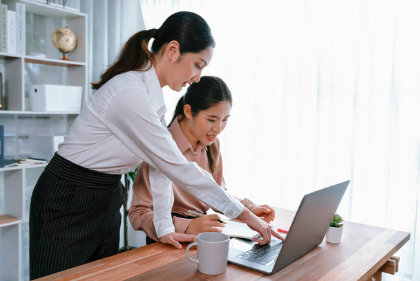 Two young office lady colleagues collaborating in modern office workspace, engaging in discussion and working together on laptop, showcasing their professionalism as modern office worker. Enthusiastic - Photo, Image