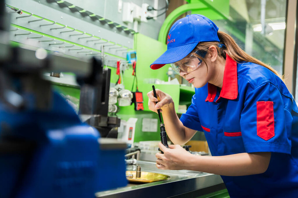 A female diesel engine mechanic in a blue uniform is working at the garage. Inspect and maintain the fuel pressure booster pump system and common rail injectors. - Fotó, kép