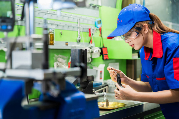 A female diesel engine mechanic in a blue uniform is working at the garage. Inspect and maintain the fuel pressure booster pump system and common rail injectors. - 写真・画像