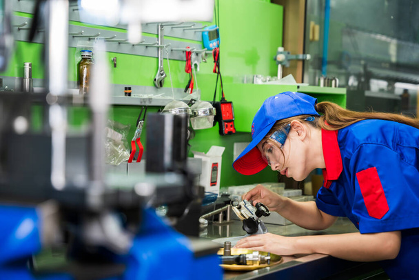 Een vrouwelijke dieselmotor monteur in een blauw uniform werkt in de garage. Inspecteren en onderhouden van het brandstofdrukverhogingspompsysteem en de injectoren van de gemeenschappelijke rail. - Foto, afbeelding
