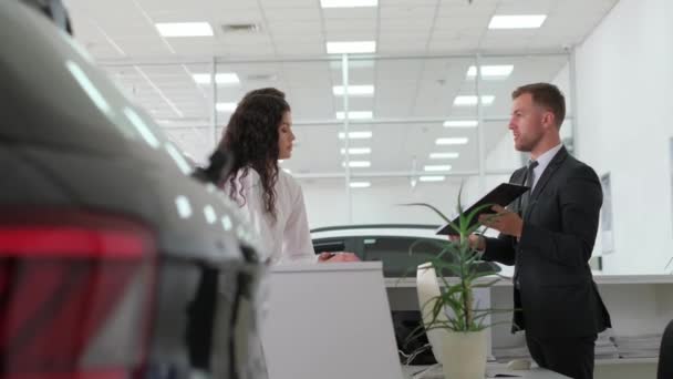 A young couple signs an order for the purchase of a car at the companys office. A car dealer works with a European couple at a car dealership and talks about buying a new car. Salesman. - Felvétel, videó