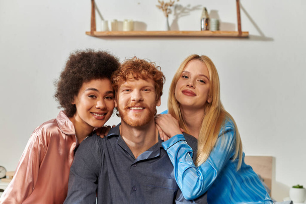 polyamory concept, open relationship, polygamy, portrait of three adults, happy redhead man and multicultural women in pajamas looking at camera, cultural diversity, acceptance, bisexual  - Photo, Image
