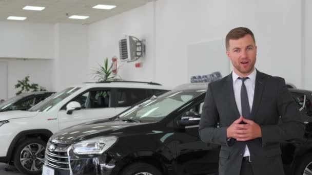 Portrait of handsome European car salesman posing at workplace in car dealership, dealership manager talking about new car. - Felvétel, videó