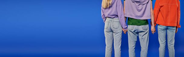 polygamy, back view of polyamory three people, young man and women holding hands on blue background, studio shot, denim fashion, love triangle, cropped shot, bonding, banner  - Photo, Image