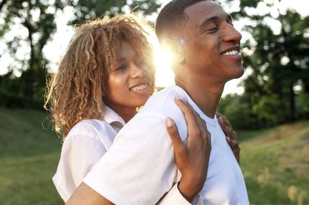 happy young african american couple standing together in the park and hugging, curly girl hugging her boyfriend and smiling, love and care concept - Foto, Imagen