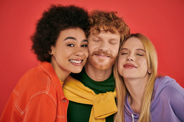 polyamorous concept, portrait of young man and multicultural women on coral background, studio shot, vibrant colors, love triangle, bonding and acceptance, happy polygamy lovers  - Photo, Image