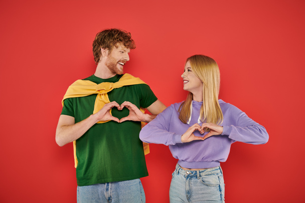 young couple looking at each other on coral background, showing heart sign with hands vibrant colors, stylish outfits, modern family, handsome man and beautiful woman, bonding and love, togetherness  - Photo, Image