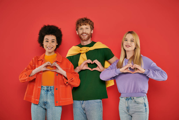 open relationship, polygamy concept, three interracial lovers showing heart sign with hands on coral background, cultural diversity, polyamorous, happy multiethnic people looking at camera  - Фото, изображение