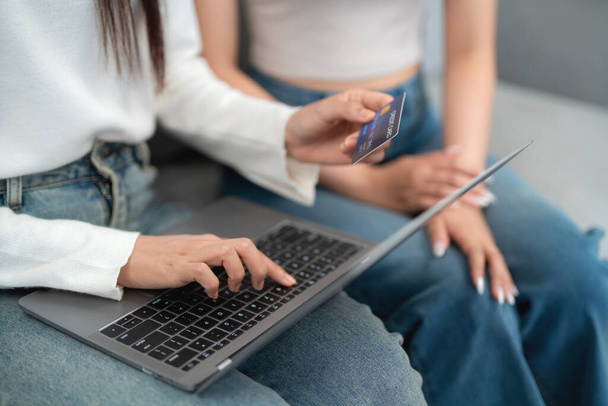 Дві азіатські молоді жінки купують онлайн покупки на ноутбуці з кредитною карткою, сидячи разом на дивані у вітальні. інтернет концепція шопінгу. - Фото, зображення