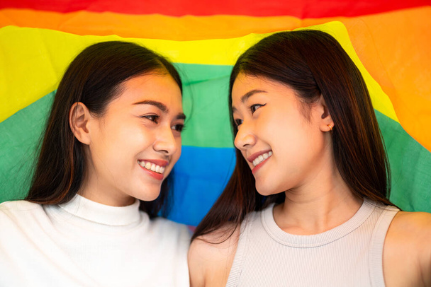 Asian couple sit eye-to-eye over a rainbow flag in protest to show their support. Lesbian rainbow flag. Lesbian couple love moments happiness concept. - Photo, Image